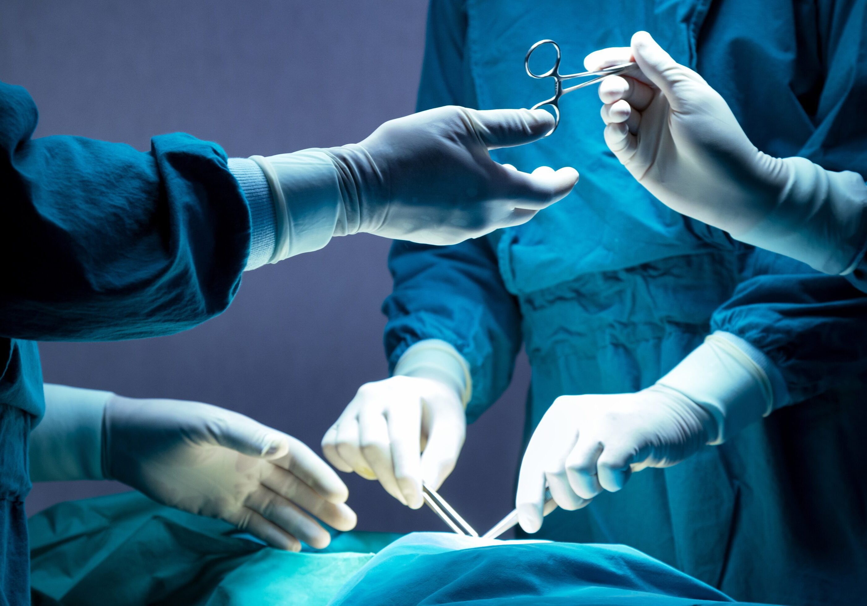 doctor and nurse medical team are performing surgical operation at emergency room in hospital. assistant hands out scissor and instruments to surgeons during operation.